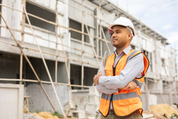 istock Confident engineer handsome man standing arms crossed at modern home building construction. Architect with white safety helmet at construction site. 1410958231