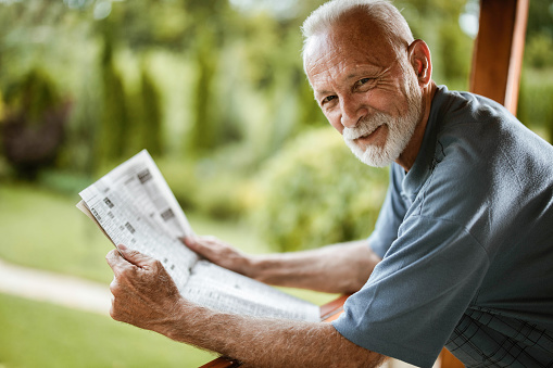 Closeup portrait of serious senior handsome man reading newspaper, having coffee break and sitting at table