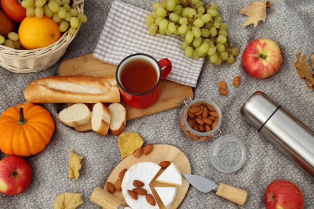 Blanket with picnic basket, snacks and autumn leaves, flat lay