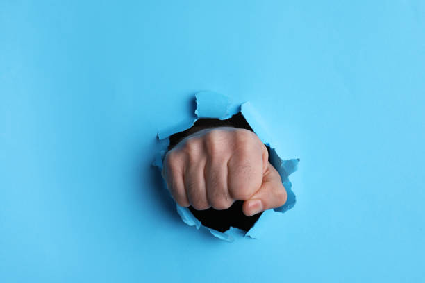istock Man breaking through light blue paper with fist, closeup 1410959578