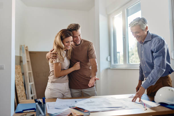 istock Happy embraced couple analyzing blueprints with an architect. 1410961224