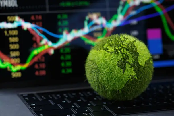 Photo of Green Globe on laptop keyboard with Stock graph on the laptop screen. Green business concept. Carbon efficient technology. Digital sustainability. future green energy innovation business trend.