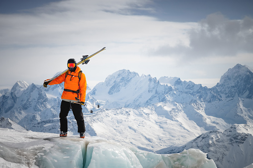 Portrait of a young skier with skis on his shoulder. It stands high in the mountains on a glacier against the backdrop of high mountains. The concept of freeride and backcountry in the highlands.