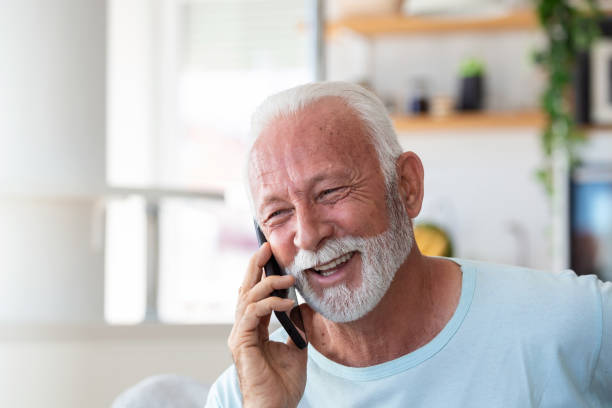 istock Senior man talking on mobile phone at home. Laughing senior man talking on a cellphone while relaxing in a chair in his living room 1410966351