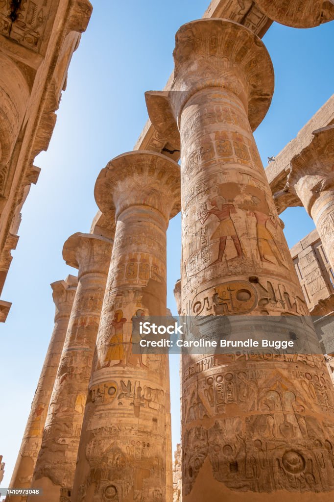 Pillars of the Karnak Temple, Luxor, Egypt Karnak Temple, Luxor, Egypt - July 26, 2022: The Karnak Temple Complex, commonly known as Karnak  comprises a vast mix of decayed temples, pylons, chapels, and other buildings near Luxor, Egypt. Construction at the complex began during the reign of Senusret I (reigned 1971–1926 BCE) in the Middle Kingdom (around 2000–1700 BCE) and continued into the Ptolemaic Kingdom (305–30 BCE), although most of the extant buildings date from the New Kingdom. 

It is part of the monumental city of Thebes (Luxor), and in 1979 it was inscribed on the UNESCO World Heritage List along with the rest of the city. Egypt Stock Photo
