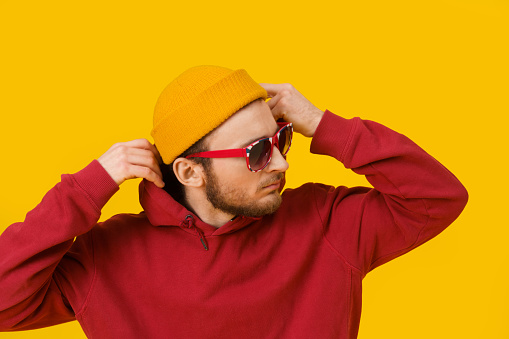 Close up portrait of pensive young man in casual wear in sunglasses posing sideways on yellow background. Stylish bearded smart hipster man casual look. Thoughtful guy on yellow background.