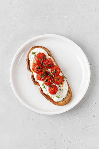 Toast, snack, bruschetta with ricotta cheese, cream cheese and baked tomatoes cherry on white plate. Healthy vegetarian sandwiches with whole grain bread. Top view.