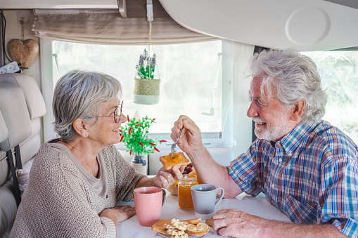 Beautiful caucasian senior couple in travel vacation leisure inside a camper van dinette enjoying breakfast together looking into each other eyes