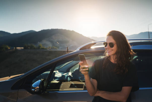 Young beautiful woman traveling by car in the mountains using smartphone at sunset, summer vacation and adventure stock photo