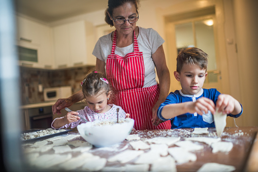 Grandmother and grandchildren preparing food at home.