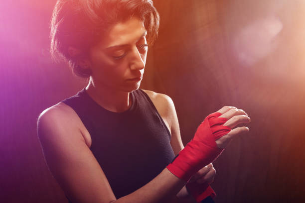 Fit and muscular female fighter getting ready for fight. Wrapping her hands in a protective boxing bandage before sports training