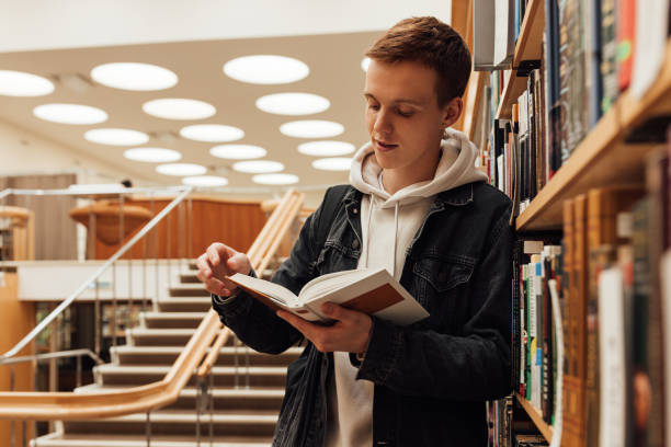 istock College student holding a book in library. Young guy leafing through a book. 1410981609