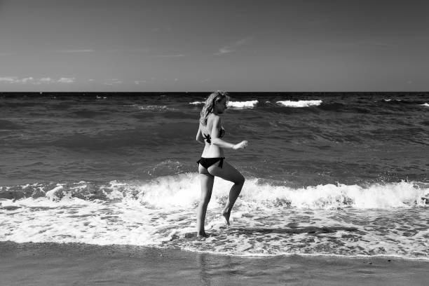 single happy young woman in swimsuit walking at sea surf with splashes