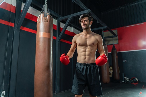 Photo of a young and handsome boxer with muscular build body with red gloves training in a gym