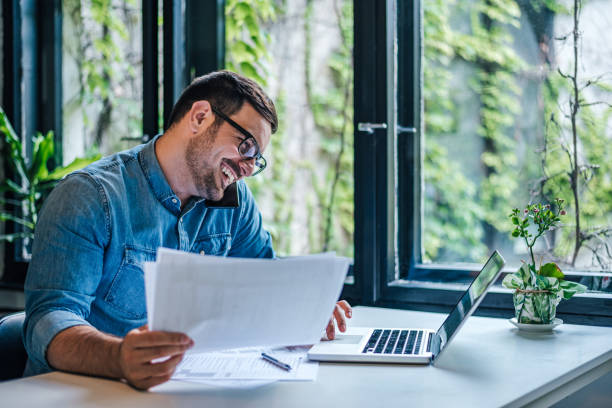 istock Happy freelancer with documents talking on smart phone and using laptop at home. 1410991425