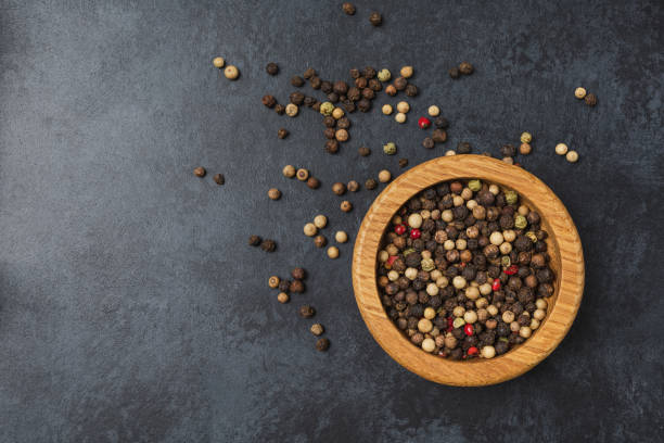 istock Pepper in wooden bowl on dark black stone table with copy space. 1410992693