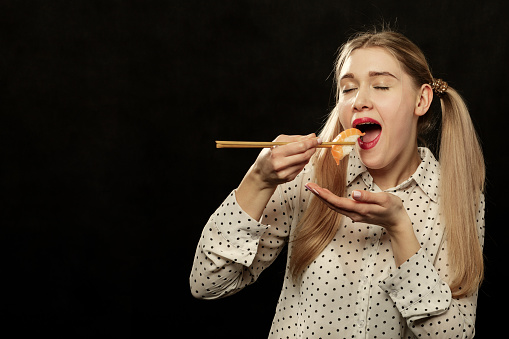 happy young fun woman eats sushi on black background with copy space