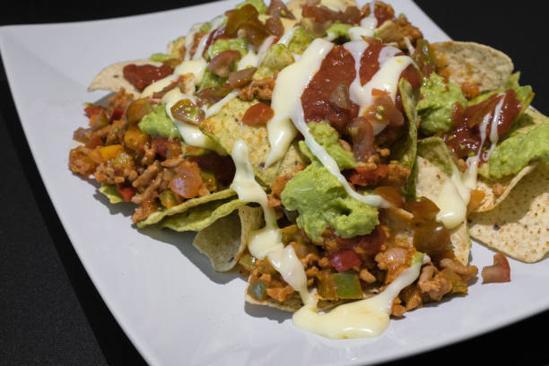 istock Nachos with minced meat, pepper, guacamole and melted cheese on a plate on a black table 1410996891
