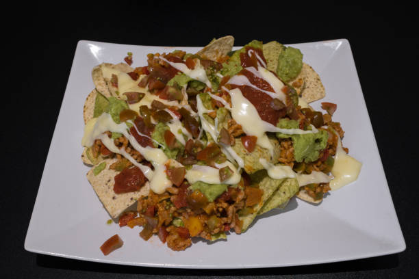 istock Nachos with minced meat, pepper, guacamole and melted cheese on a plate on a black table 1410996900
