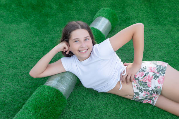 人工芝の新しいロールに横たわって若い笑顔の白人の女の子。ニース人工芝は、敷設する準備ができて - fire retardant ストックフォトと画像