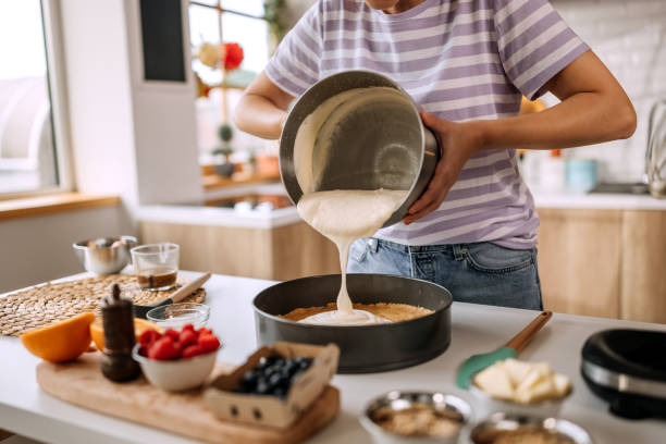 Unrecognisable woman pouring cheesecake filling into baking tin
