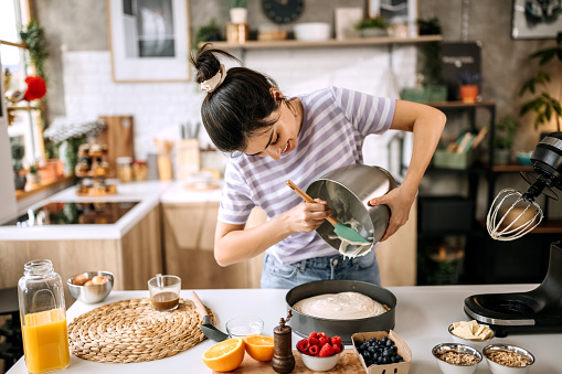 Young beautiful woman pouring cheesecake filling into baking tin