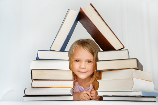 A little girl looks into the camera from the stack of books. back to school.