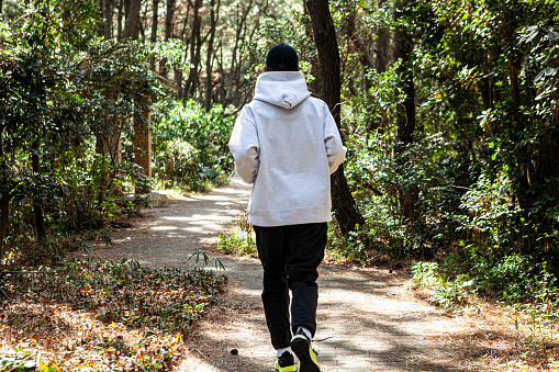 Back shot of a middle-aged Asian male running in the forest in daytime