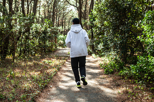Back shot of a middle-aged Asian male running in the forest in daytime