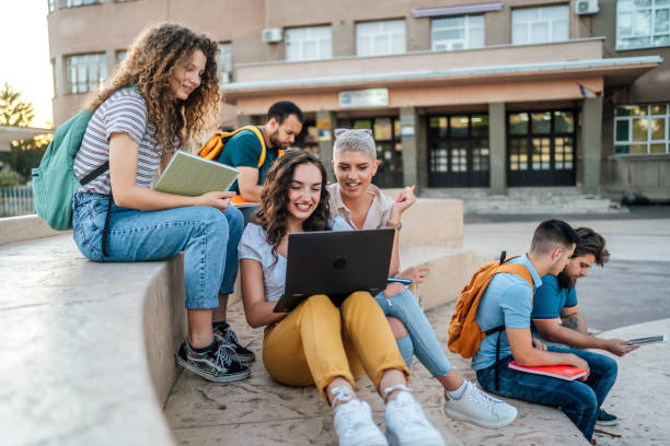 Students on campus Group of students sitting outdoors, hanging out, talking and using laptop adult student stock pictures, royalty-free photos & images