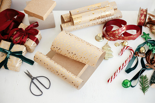 Wrapping stylish christmas gifts. Modern gift boxes, red and green ribbons, golden wrapping paper, ornaments and scissors on white background. Merry Christmas! Atmospheric winter time