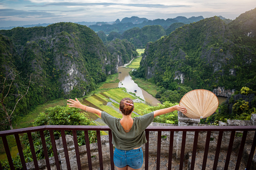 Tourist with outstretched arms in Ninh Binh, Vietnam. Happy tourist in Vietnam. Young woman with outstretched arms. Vietnamese woman with hat