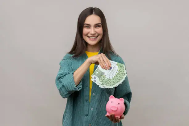 Photo of Attractive smiling woman holding euro banknotes and piggy bank, savings, high rate deposit.