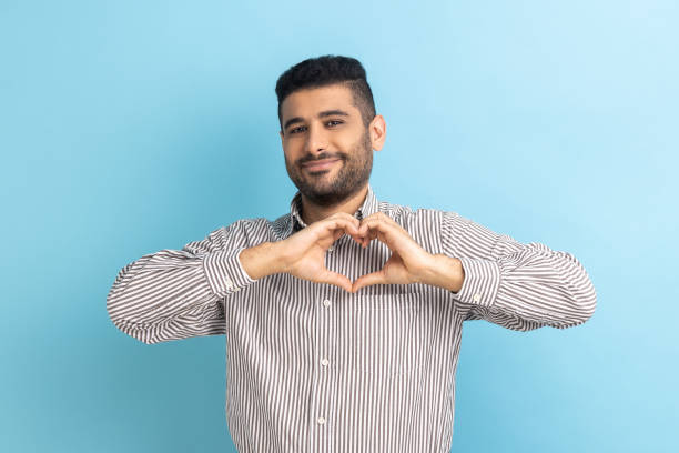 businessman with beard standing, showing heart shape making with hands, looking at camera with love. - made man object imagens e fotografias de stock