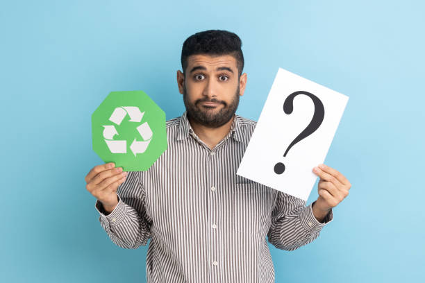 Doubtful confused businessman standing holding green recycling sign and paper with question mark stock photo