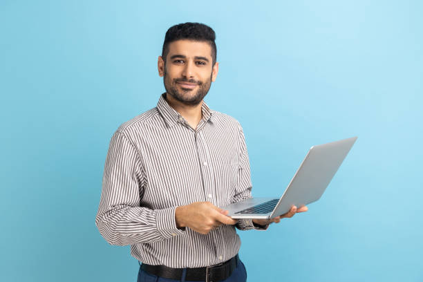 istock Smiling man freelancer with beard standing and holding laptop, satisfied with teleworking. 1411002091