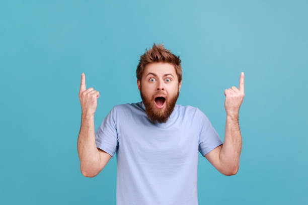 istock Man pointing up at copy space and looking surprised, showing blank wall for idea presentation. 1411002129