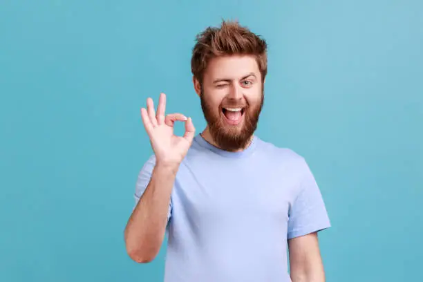 Photo of Man in blue T-shirt showing okay sign, success sign, satisfied with good service, looking at camera.