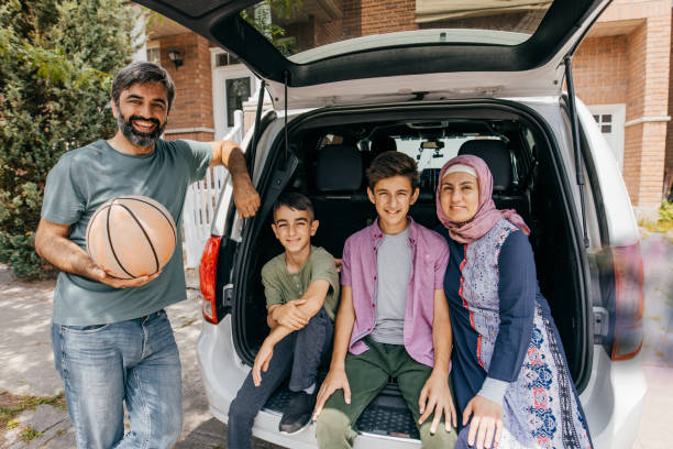 Happy parents and their kids enjoying while going on a trip by car. The view is through glass.