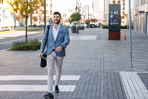 A young Caucasian businessman in an elegant jacket is cheerfully taking a morning walk to work.