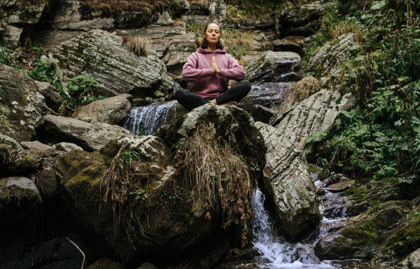 istock Serene woman meditating on the stone next to a mountain spring 1411007840
