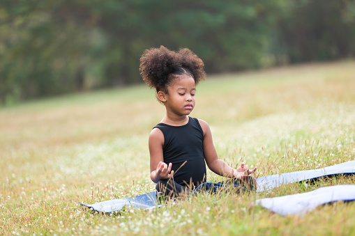Child little girl doing meditate yoga asana on roll mat with eyes closed in park. Kids girl practicing doing yoga outdoor