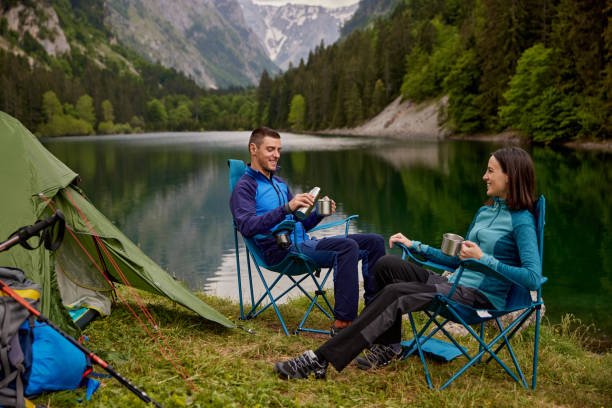 ein abenteuerlustiges junges paar auf seinem campingplatz trinkt kaffee - campingstuhl stock-fotos und bilder