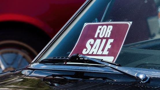 A FOR SALE sign behind the windshield on the old car