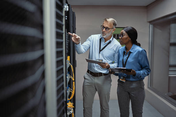 istock A male computer engineer and a female network analyst monitoring firewalls and doing diagnostics on hard drives. Two IT technicians checking on working databases inside a dark server storage room. 1411009461