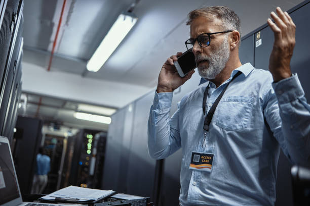 Frustrated IT professional arguing on the phone while working in a server room. Male computer engineer making a call, disagreeing with a client and diagnosing or assessing network problems and issues
