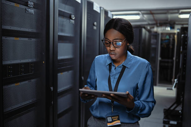 técnica de ti usando una tableta en una sala de servidores. joven programador que repara un sistema informático bloqueado o fallido durante el mantenimiento en un centro de datos. ingeniero que actualiza el software de seguridad en una máquina - network server black computer network rack fotografías e imágenes de stock