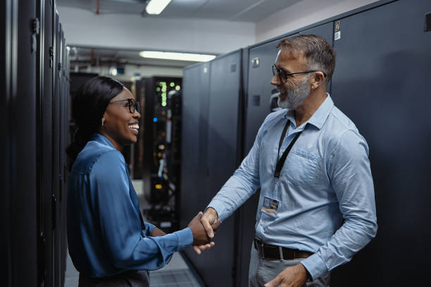 Two IT technicians greeting with a handshake, welcome to assist in a server room. Professional computer engineers shaking hands for promotion and success, and smiling after a completed job well done stock photo