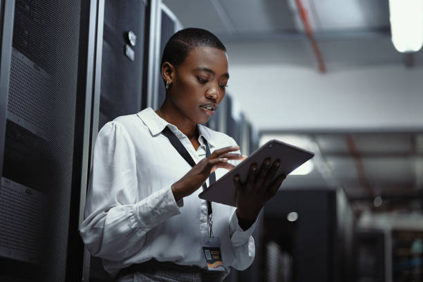 técnico de ti utilizando una tableta digital en una sala de servidores. programadora arreglando un sistema informático y una red mientras realiza el mantenimiento en un centro de datos. ingeniero que actualiza el software de seguridad en una máquina - network server black computer network rack fotografías e imágenes de stock