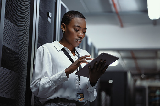 IT technician using a digital tablet in a server room. Female programmer fixing a computer system and network while doing maintenance in a datacenter. Engineer updating security software on a machine